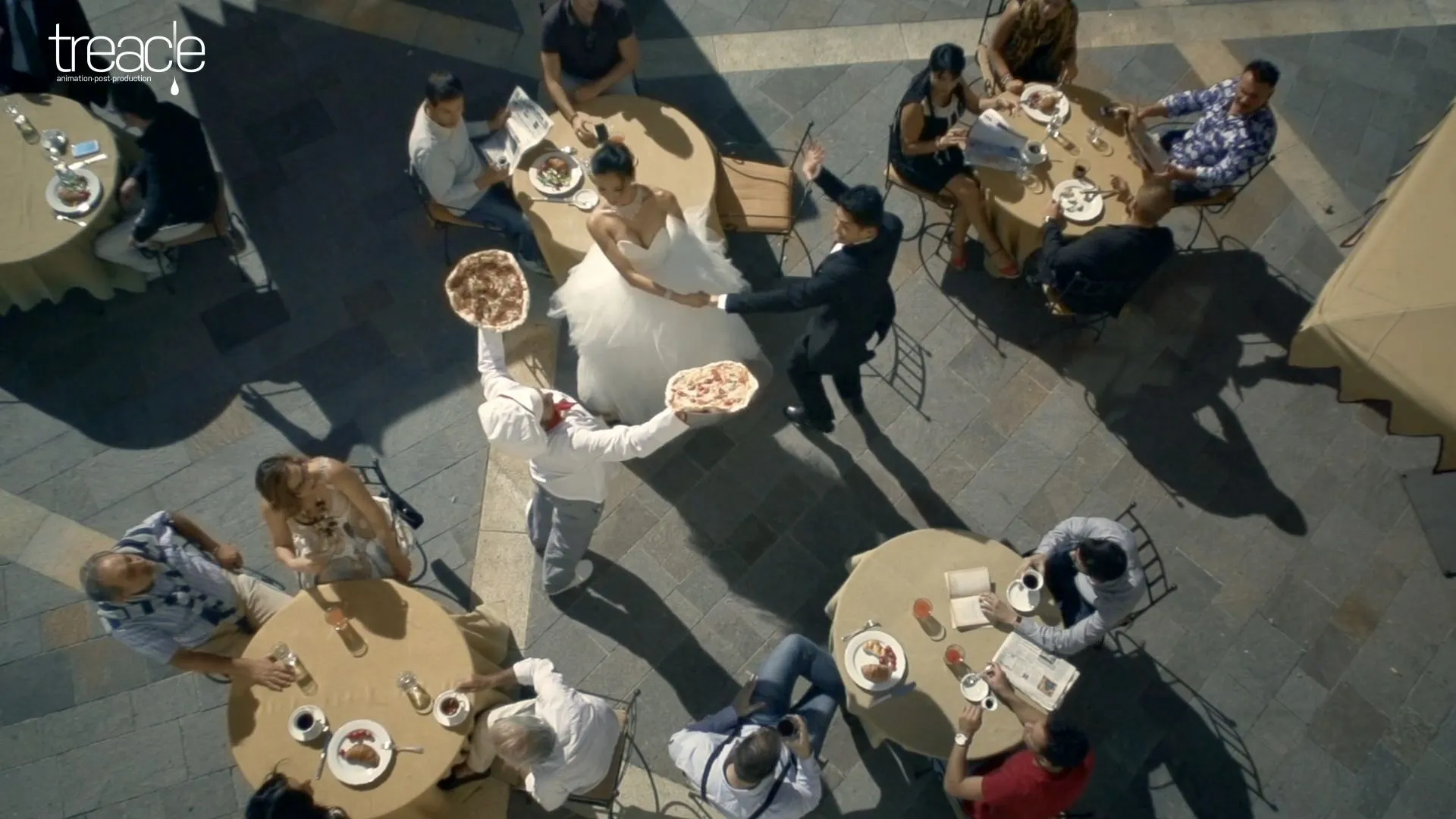 A bride and groom run past a chef with a pizza in each hand.